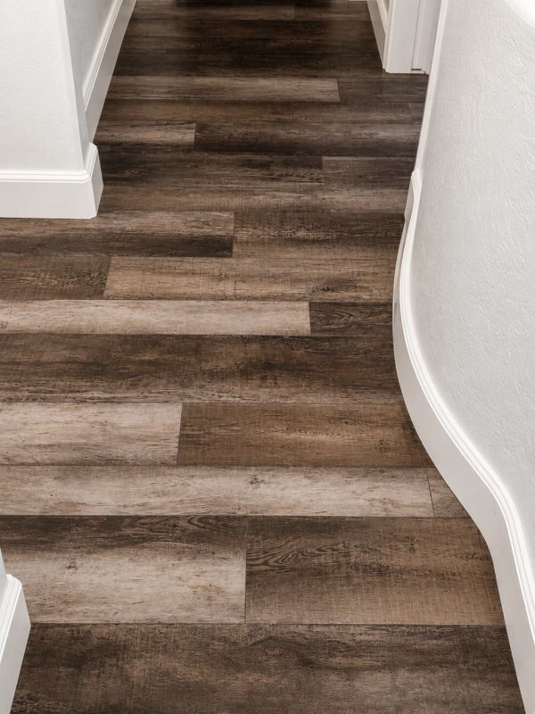 Dark wood patterned flooring in a hallway with white baseboards.