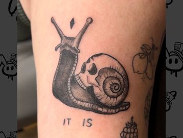 Tattoo of a snail with a skull shell and text 'IT IS'.
