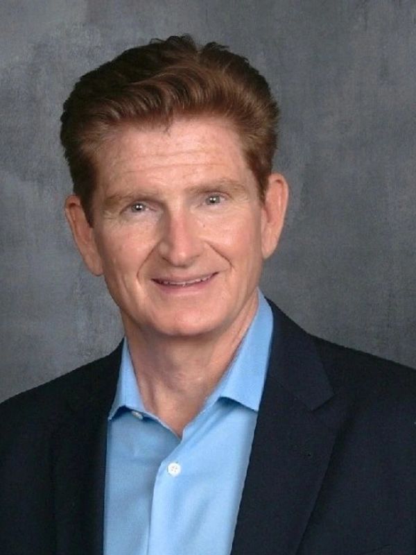 Smiling man in a blue shirt and dark blazer against a gray background.Pre IPO, IPO