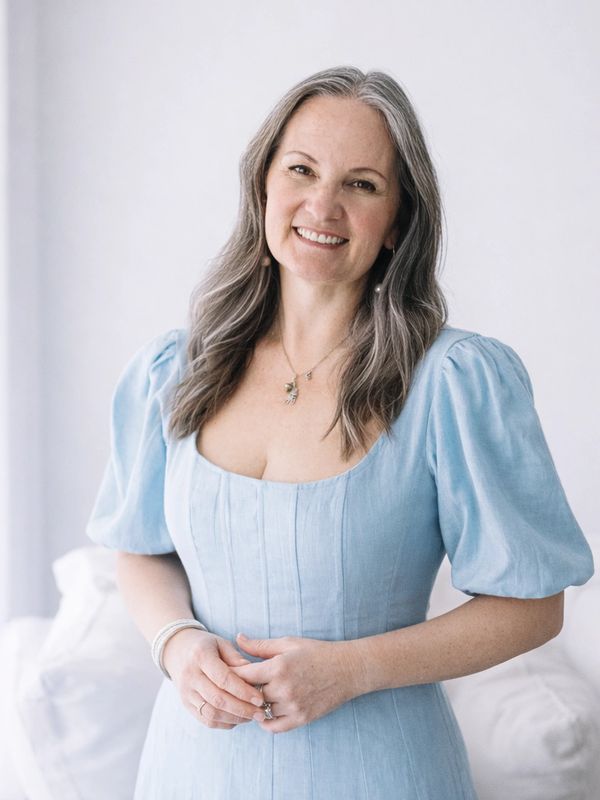 Smiling woman in a light blue dress standing indoors with soft natural light.