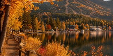 Autumn foliage lines a lakeside path with mountains in the background.