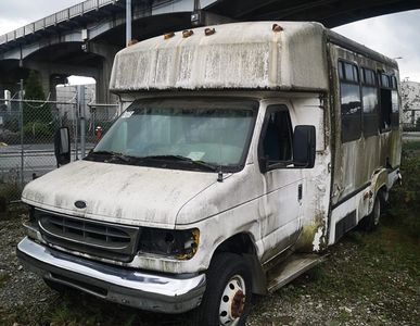 A dirty old white van parked under a bridge. 