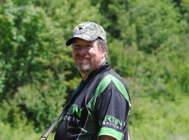 Man in a camo hat and black-green shirt outdoors.