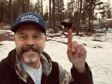 Man with a cap pointing at a moose in a snowy forest.