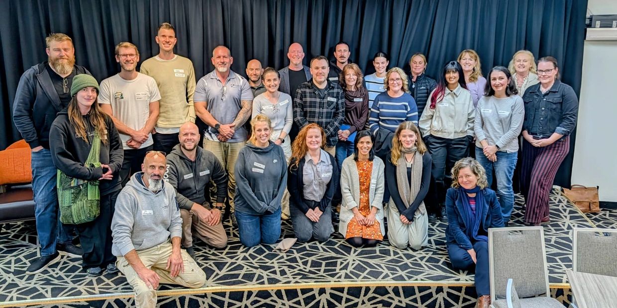 Group photo of diverse adults posing indoors on patterned carpet.