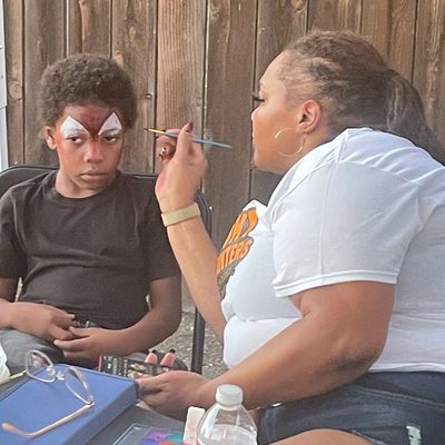 DeeHeart painting a child’s face during a community event as part of the outreach program.