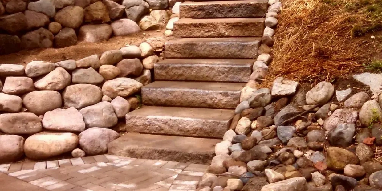 concrete steps with a paver pad and boulder retaining walls