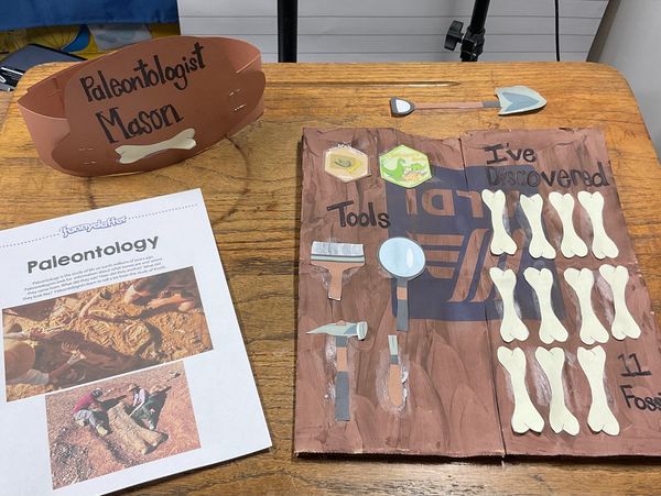 A paleontology project display with tools, fossil bones, and a paper titled "Paleontology".