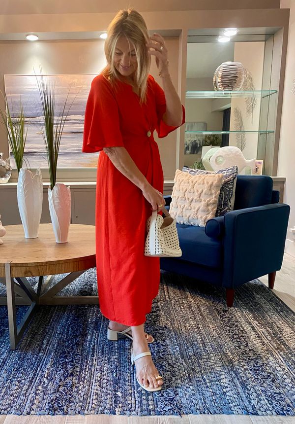 Woman in a red dress holding a white handbag, standing in a stylish living room.