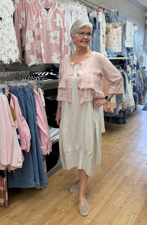 Elderly woman modeling a light dress and pink cardigan in a clothing store.