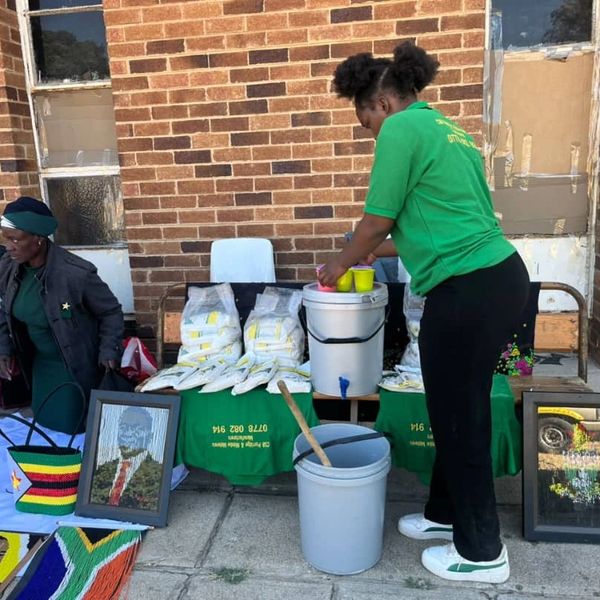 Women selling traditional crafts and packaged goods outside a brick building.