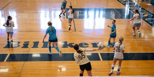 Indoor volleyball game with players in action on a wooden court.