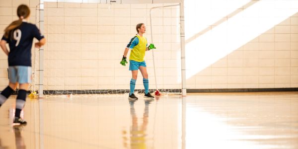 Youth goalkeeper preparing to defend the goal indoors.
