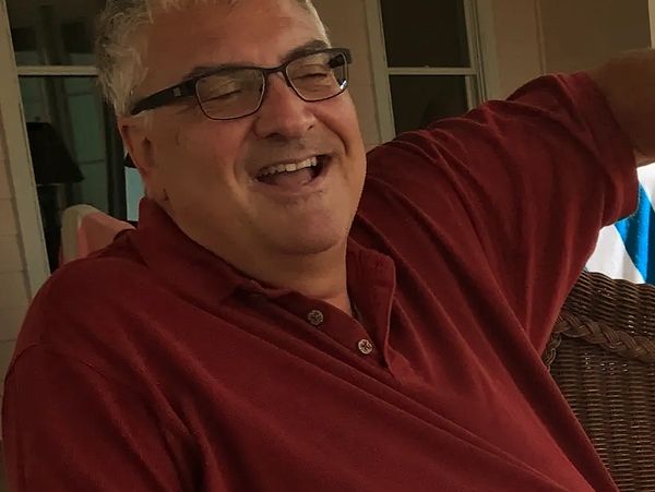 A joyful man in glasses and a red shirt laughing heartily.