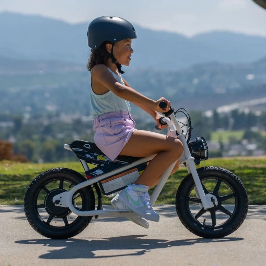 Child riding a small electric bike wearing a helmet.