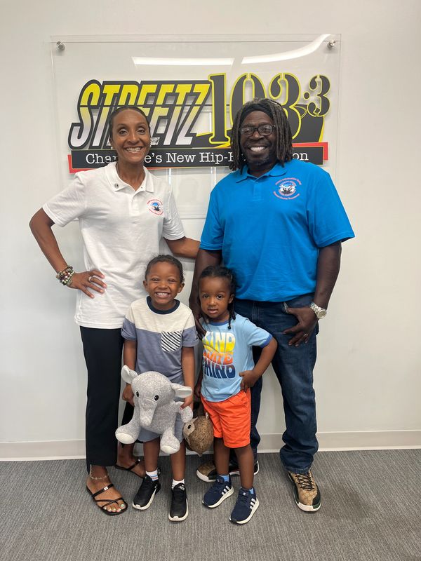 Smiling family of four posing in front of a Streetz 103.3 radio station sign.