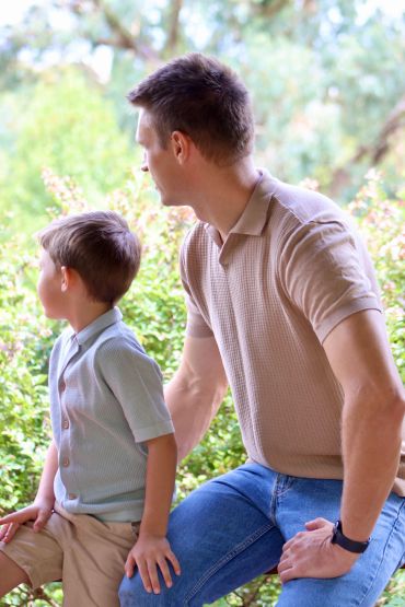 Father and son sitting outdoors looking away.