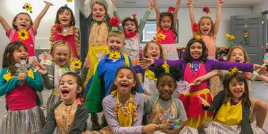 Cheerful children in colorful costumes posing excitedly with flowers and crafts.