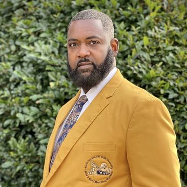 Man wearing a mustard yellow blazer with a patterned tie, standing outdoors.