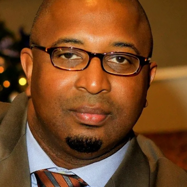 Close-up of a man wearing glasses and a suit with a striped tie.