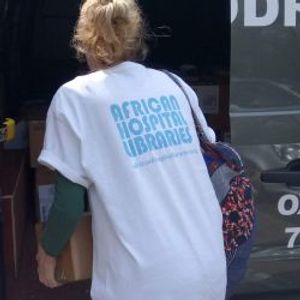 Person wearing an African Hospital Libraries shirt entering a building.