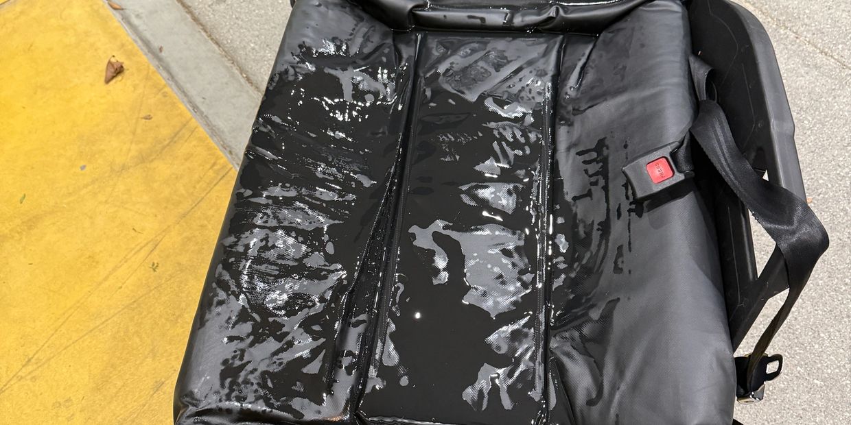 Wet black car seat with seatbelt on a concrete surface.