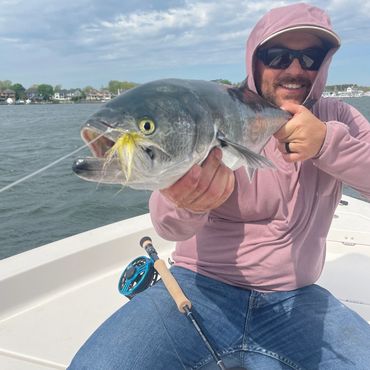 Man holding a freshly caught fish on a boat with a fishing rod.