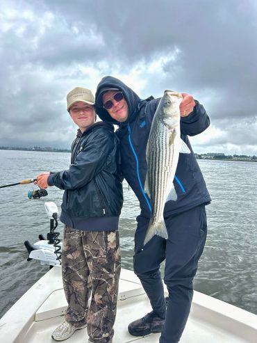 Two people on a boat holding a large fish on a cloudy day.