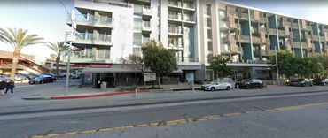 Modern apartment building with shops on the ground floor along a street.