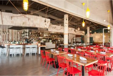 Modern restaurant interior with red chairs and wooden tables.