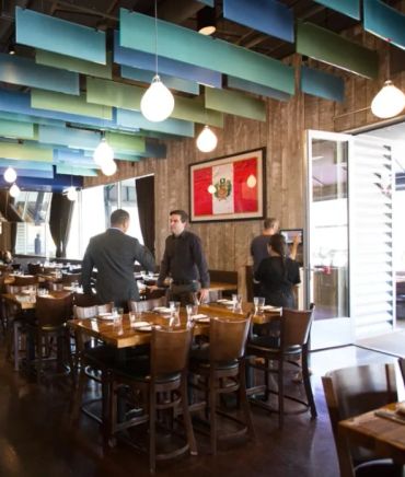 Modern restaurant interior with wooden tables and colorful ceiling panels.