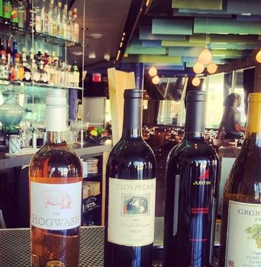 Four bottles of wine displayed on a bar counter in a cozy restaurant.