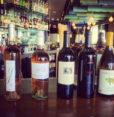 Four bottles of wine displayed on a bar counter in a cozy restaurant.