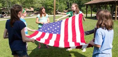 Girls outdoors holding an American flag together.