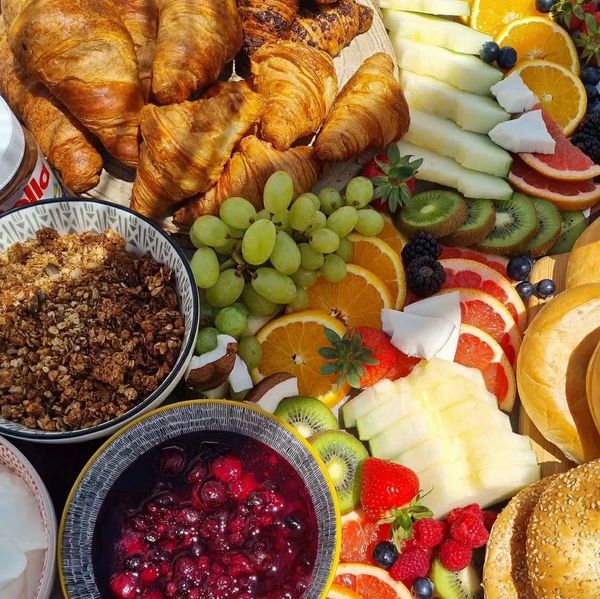 A colorful breakfast spread with croissants, fresh fruit, granola, and berry compote.