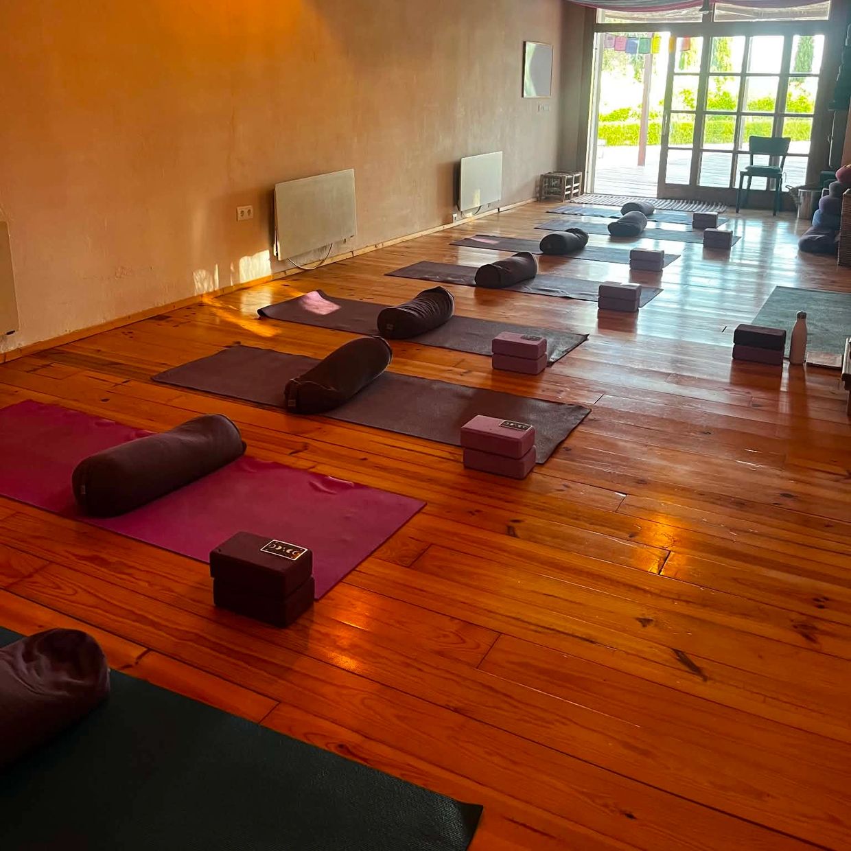 A serene yoga studio with mats and bolsters neatly arranged on a wooden floor.