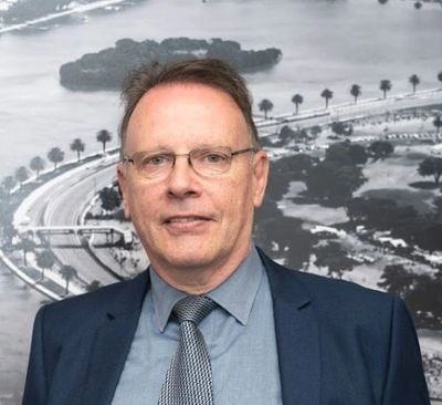 Man in suit and tie standing in front of a black-and-white aerial cityscape.