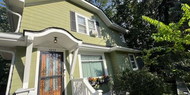 Green two-story house with white trim and a wooden front door under a sunny sky.