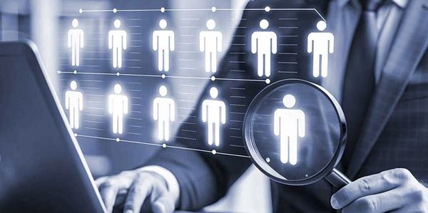 Businessman using magnifying glass to select a digital person icon on screen.