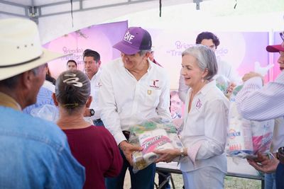 Two volunteers distribute food packages to people at a community event.
