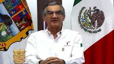Hombre dando un discurso frente a banderas oficiales.
