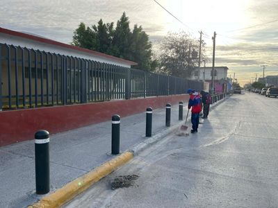 Two people walking along a street with black bollards and a fence.