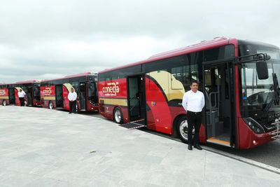 Several red buses parked with drivers standing beside them.