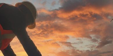 a worker laying brick on a building with a sunset in the background 