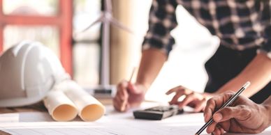 A set of engineering plans on a table with two people working on them 