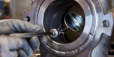 A worker inspects a metal component using a precision measuring tool.