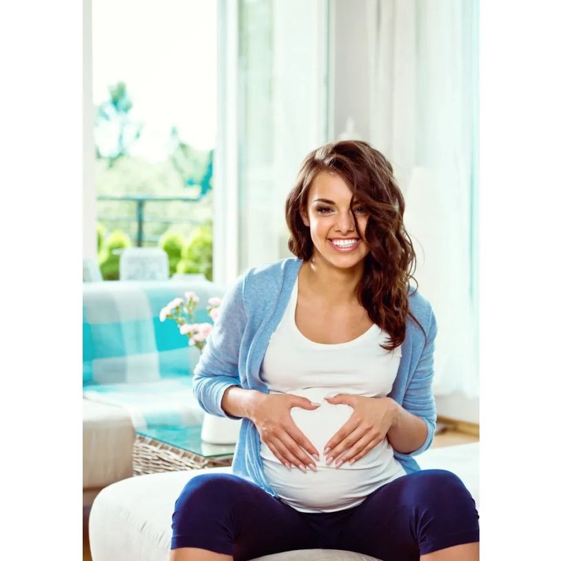 A pregnant woman smiling and making a heart shape with her hands over her belly
