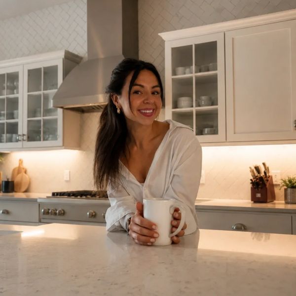Woman smiling in kitchen holding a white mug.
