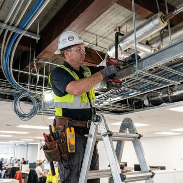 Electrician working on wiring in office ceiling.