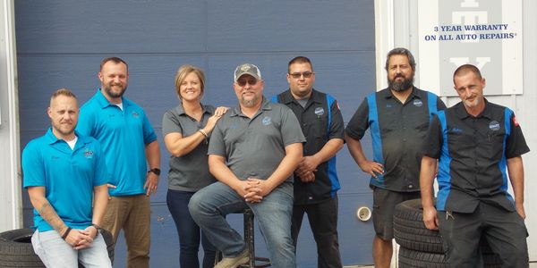 Quality Auto Mart employees posing outside a business with tires and uniforms.